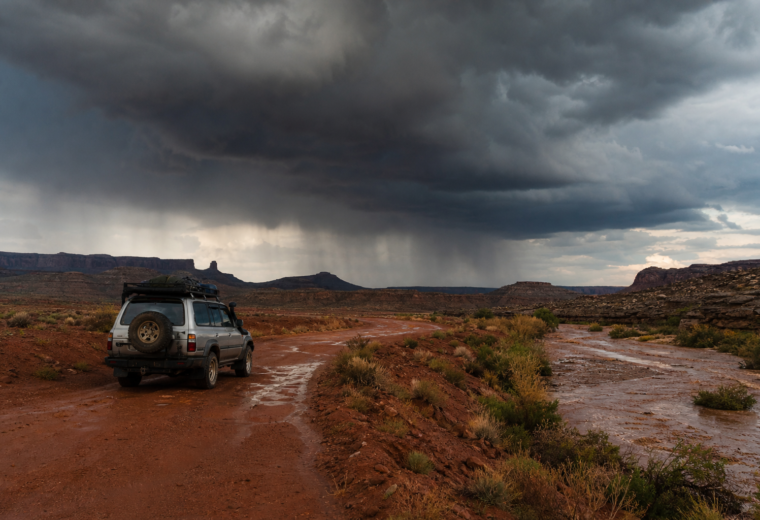Overland vehicle paused near a desert wash as monsoon storm clouds build over a dirt road in the Southwest.